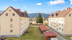 A residential building with multiple floors, a central courtyard, and a view of mountains in the background. - FarawayHomes Studio Krieglach 14 (Sommer)