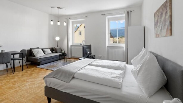 A modern bedroom with a large bed, a sofa, a desk, and a TV. - FarawayHomes Studio Krieglach 14 (Sommer)