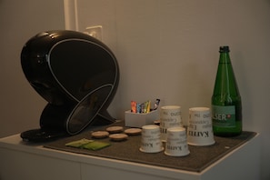 Una cafetera, una botella de vino Alser y varias tazas de café sobre una mesa.