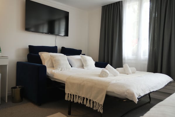Une chambre dâhĂŽtel moderne, Ă©quipĂ©e dâun lit, dâun tĂ©lĂ©viseur fixĂ© au mur et dâune fenĂȘtre avec des rideaux.