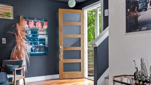 Een modern interieur met een houten deur, een ingelijste afbeelding, een stoel en een eettafel met bestek.