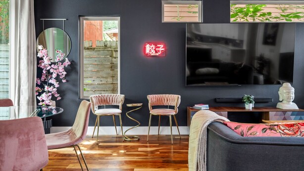 Een moderne woonkamer met een donkere muur, een ronde spiegel, twee roze fauteuils, een bank en een flatscreen-tv.