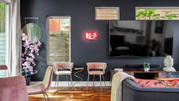 Ett modernt vardagsrum med en mörk vägg, en rund spegel, två rosa fåtöljer, en soffa och en platt-TV.