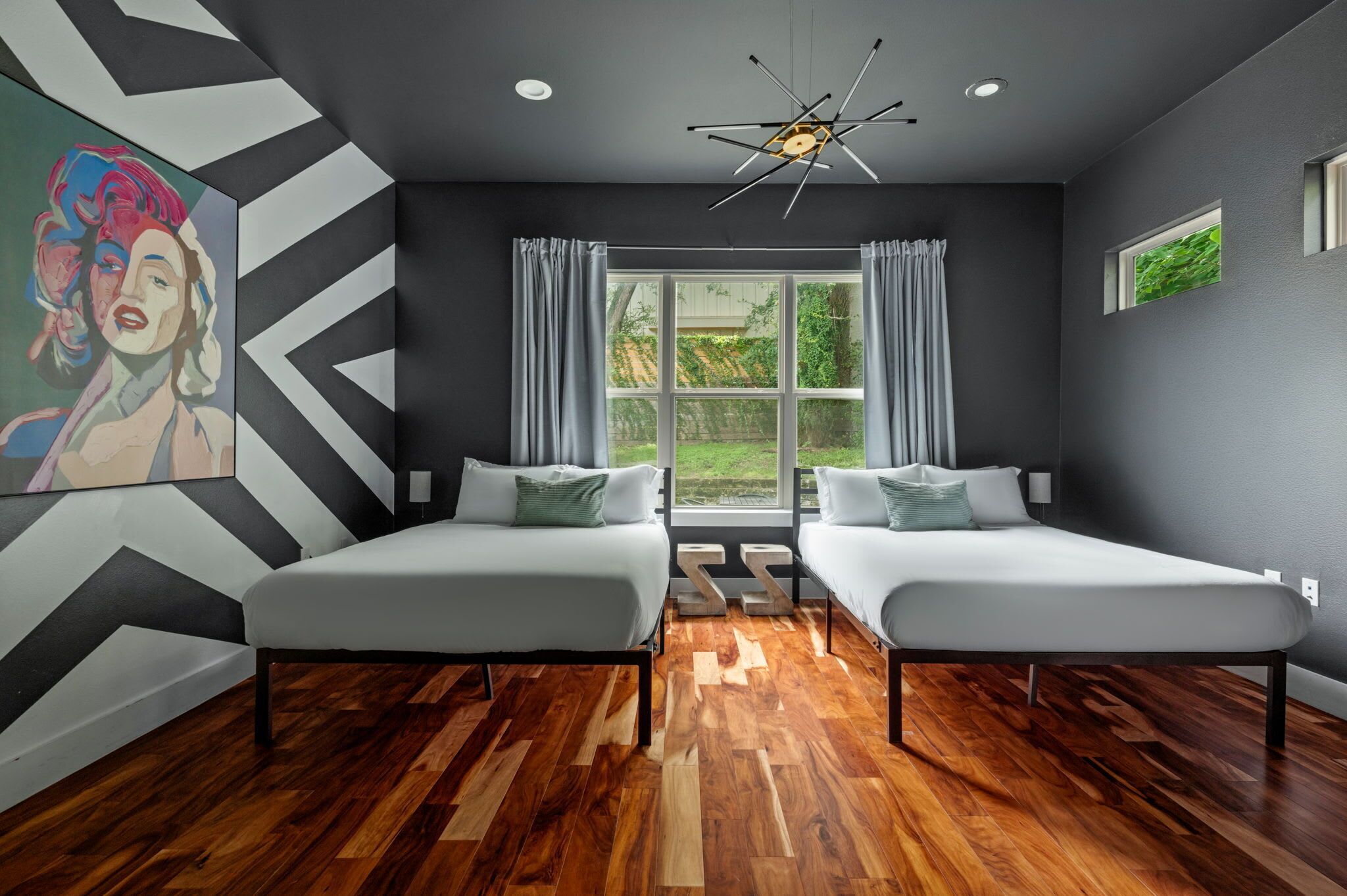 Une chambre moderne avec deux lits, une grande fenêtre et un luminaire au plafond au design original.