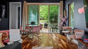 Een modern interieur met een houten vloer, een eethoek met roze stoelen, en een grote glazen schuindeur die leidt naar een terras.
