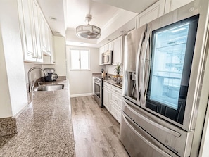 A kitchen with stainless steel appliances, a granite countertop, and white cabinetry. - Menehune Shores - 4BR Condos - Sleeps 12 (Kihei)