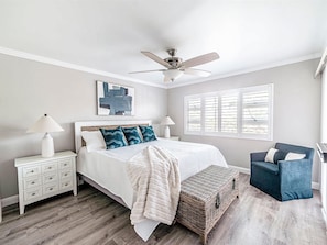 A bedroom with a bed, nightstands, a ceiling fan, a window with blinds, and a chair. - Menehune Shores - 4BR Condos - Sleeps 12 (Kihei)