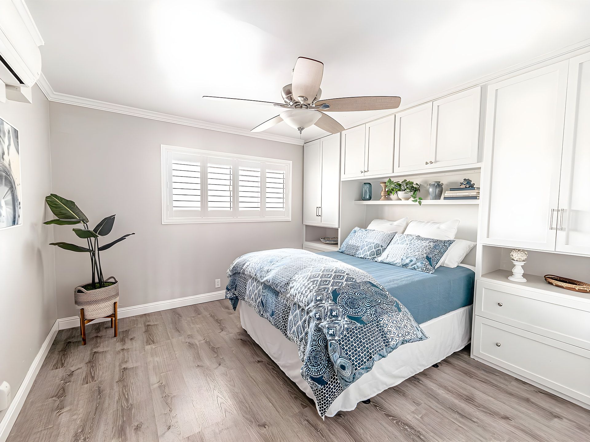 Un dormitorio con cama, ventilador de techo, armarios blancos y ventana con persianas.
