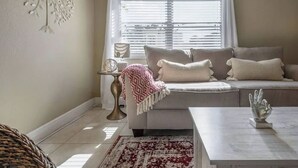 A living room with a sofa, a coffee table, a patterned rug, a decorative wall piece, and a window with blinds. - The Parkside Palm - Tampa retreat for 6 (Tampa)