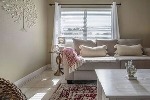 A living room with a sofa, a coffee table, a patterned rug, a decorative wall piece, and a window with blinds. - The Parkside Palm - Tampa retreat for 6 (Tampa)