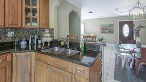 A kitchen with wooden cabinets, a tiled backsplash, a sink, and a dining area with a table and chairs. - The Parkside Palm - Tampa retreat for 6 (Tampa)