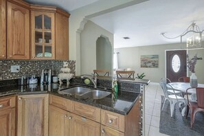 A kitchen with wooden cabinets, a tiled backsplash, a sink, and a dining area with a table and chairs. - The Parkside Palm - Tampa retreat for 6 (Tampa)
