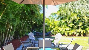 A glass-top table with white chairs and a large umbrella, surrounded by lush greenery. - The Parkside Palm - Tampa retreat for 6 (Tampa)
