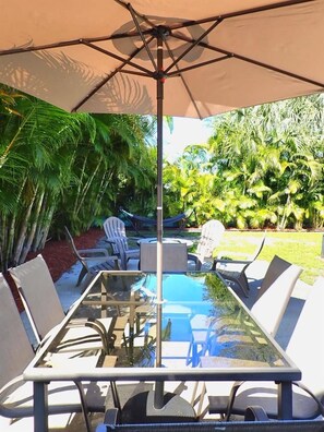 A glass-top table with white chairs and a large umbrella, surrounded by lush greenery. - The Parkside Palm - Tampa retreat for 6 (Tampa)