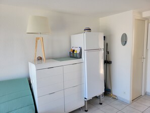 Ein kleiner Raum mit einem weißen Schrank, einer Lampe, einem Kühlschrank und einem an der Wand angelehnten Besen.