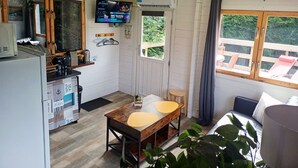 Eine kompakte Küche mit Fernseher, ein Essbereich mit Tisch und Stühlen sowie eine Sitzecke mit Blick auf Grünflächen.