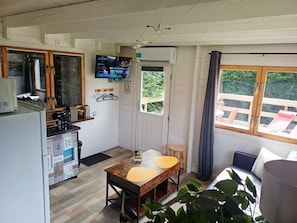 Cocina compacta con televisor, comedor con mesa y sillas, y zona de estar con vista a zonas verdes.