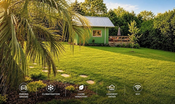 Una casa verde con techo de metal, rodeada de un césped cuidado y árboles.