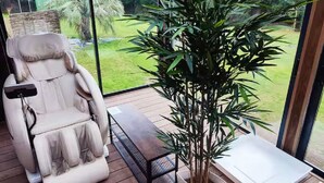 Ein Massagesessel, ein Blumentopf und ein Tisch auf einer Holzterrasse mit Blick auf einen Garten.