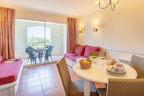 A room with a bed, a dining table with chairs, a sofa, and a balcony with chairs.