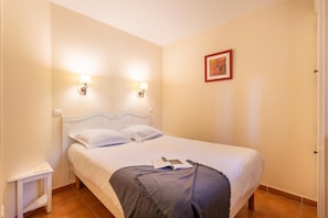 A neatly made bed with a white headboard, two wall-mounted lamps, a small bedside table, and a framed picture on the wall. - Riverfront Retreat Near Cannes (Mallemort)