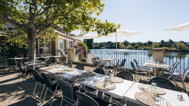 An outdoor dining area with tables and chairs, overlooking a body of water. - Riverfront Retreat Near Cannes (Mallemort)