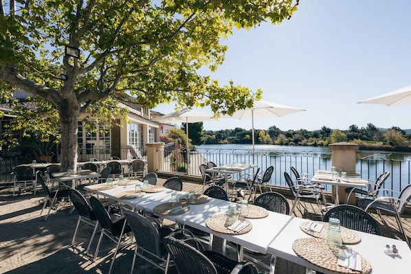 An outdoor dining area with tables and chairs, overlooking a body of water.