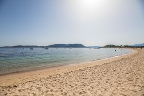 Una playa con agua cristalina, barcos y montañas a lo lejos.