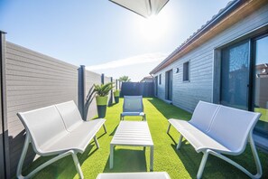 A patio with white chairs and a table, surrounded by a wooden fence and a building with large windows. - Lecci Stay With Heated Pool (Lecci)