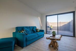 Una sala de estar moderna con un sofá color turquesa, una mesa de centro de madera y un puerta corrediza de vidrio que da a un espacio al aire libre.
