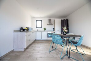 Une cuisine moderne avec des meubles blancs, un coin repas doté d’une table noire et de chaises bleues, et une fenêtre située au-dessus de l’évier.