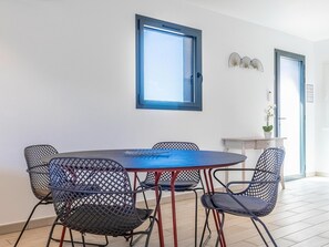 A dining area with a round table and four chairs, a window with a blue frame, and a door with a light switch. - Lecci Stay With Heated Pool (Lecci)