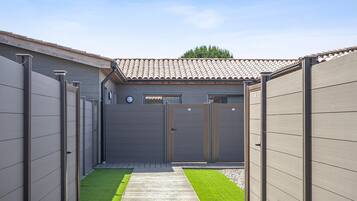 A gated backyard with a wooden deck, a small lawn, and a building with a tiled roof.