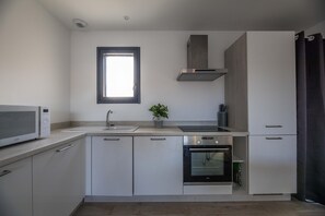 A modern kitchen with white cabinets, a microwave, a sink, a stove, and a window. - Lecci Stay With Heated Pool (Lecci)