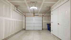 Eine Garage mit weißen Garagentüren, einer Deckenleuchte und einem Betonboden.