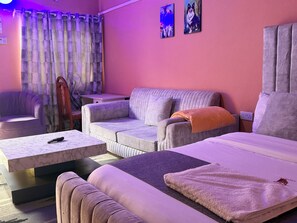 Ein Zimmer mit einer Couch, einem Sessel, einem kleinen Tisch, einem Bett und einem Vorhang.