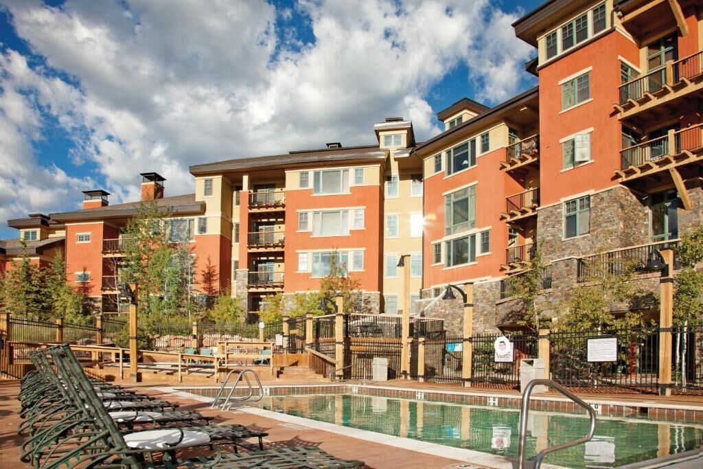 A hotel with a swimming pool, outdoor seating, and a view of the surrounding buildings.