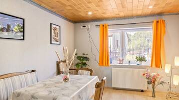 Un coin repas avec une table dressée pour deux personnes, une chaise, un radiateur et une fenêtre avec des rideaux.