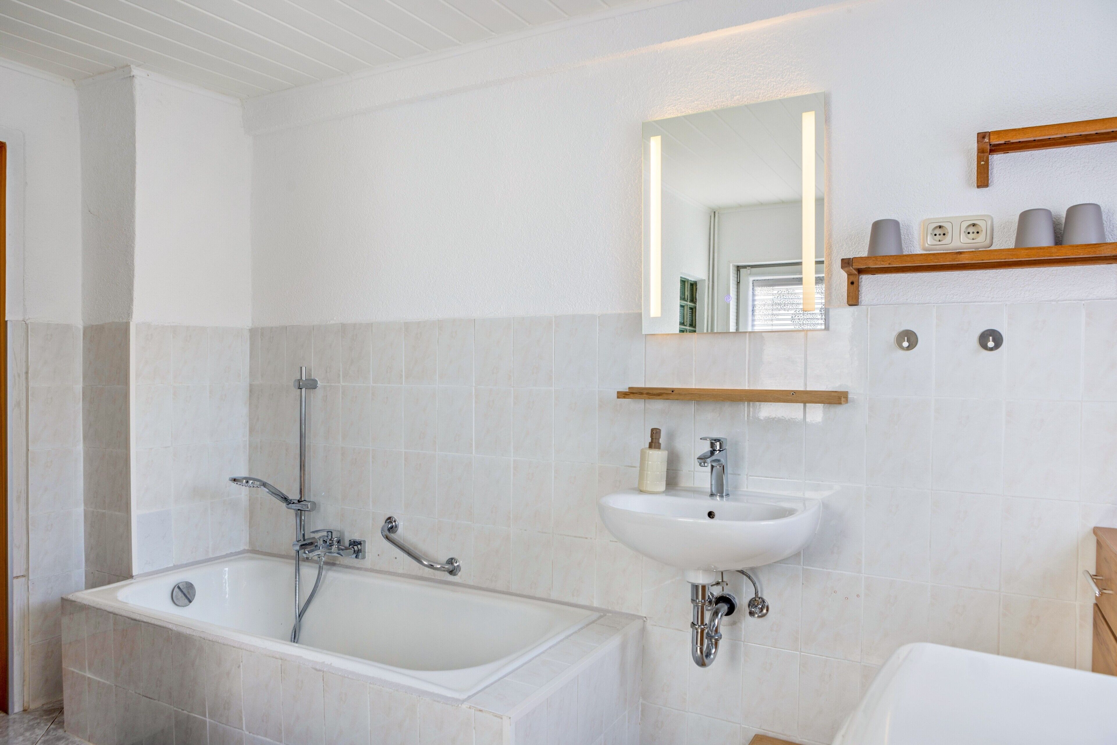 A bathroom with a bathtub, a sink, and a mirror. There are shelves above the mirror with toiletries.