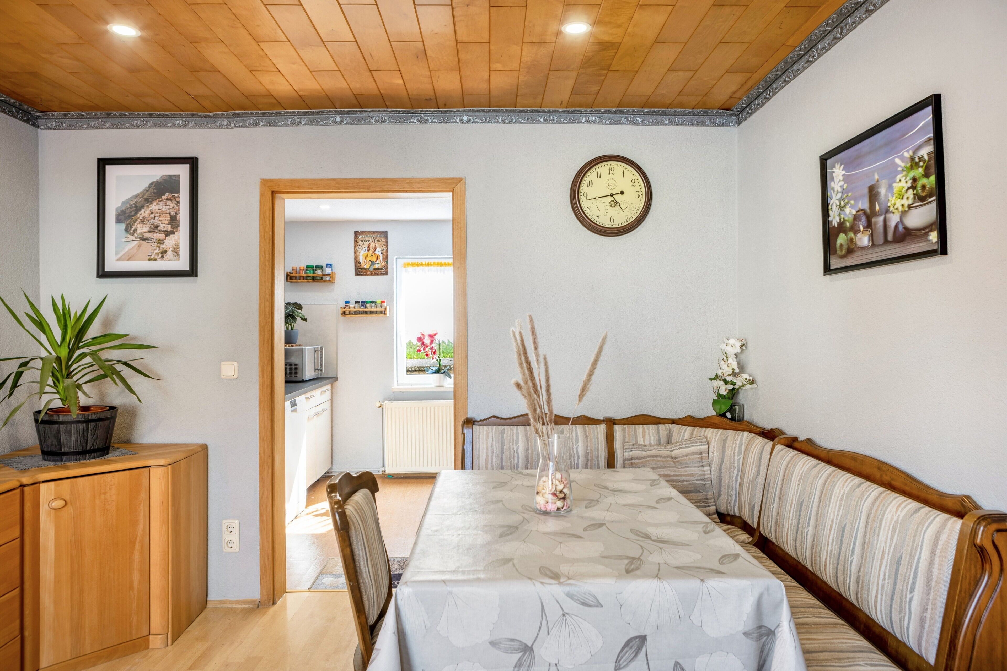 A dining area with a wooden table, benches, and a clock on the wall.