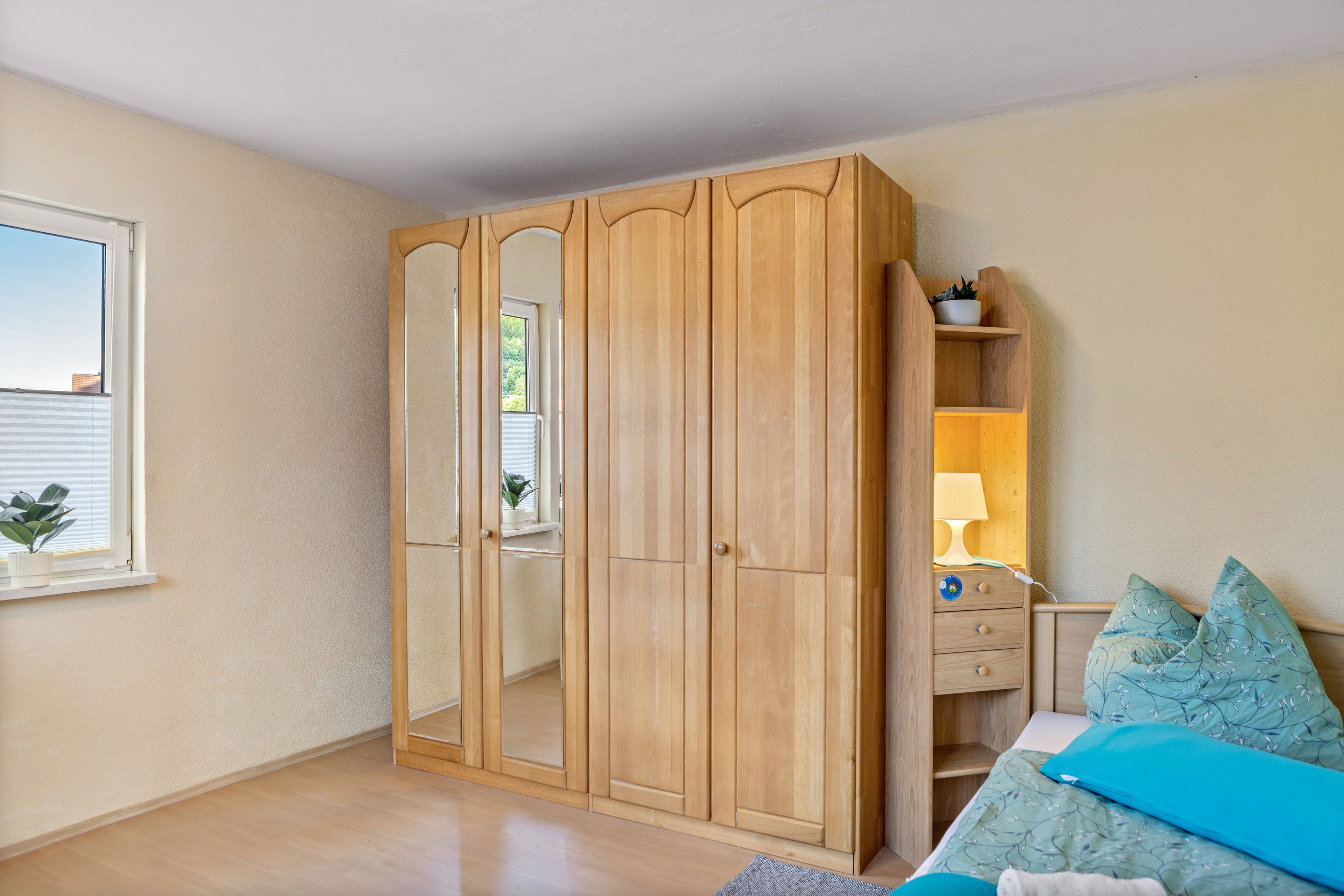 Un dormitorio con un armario de madera, una cama con almohada azul y una mesita de noche con lámpara.