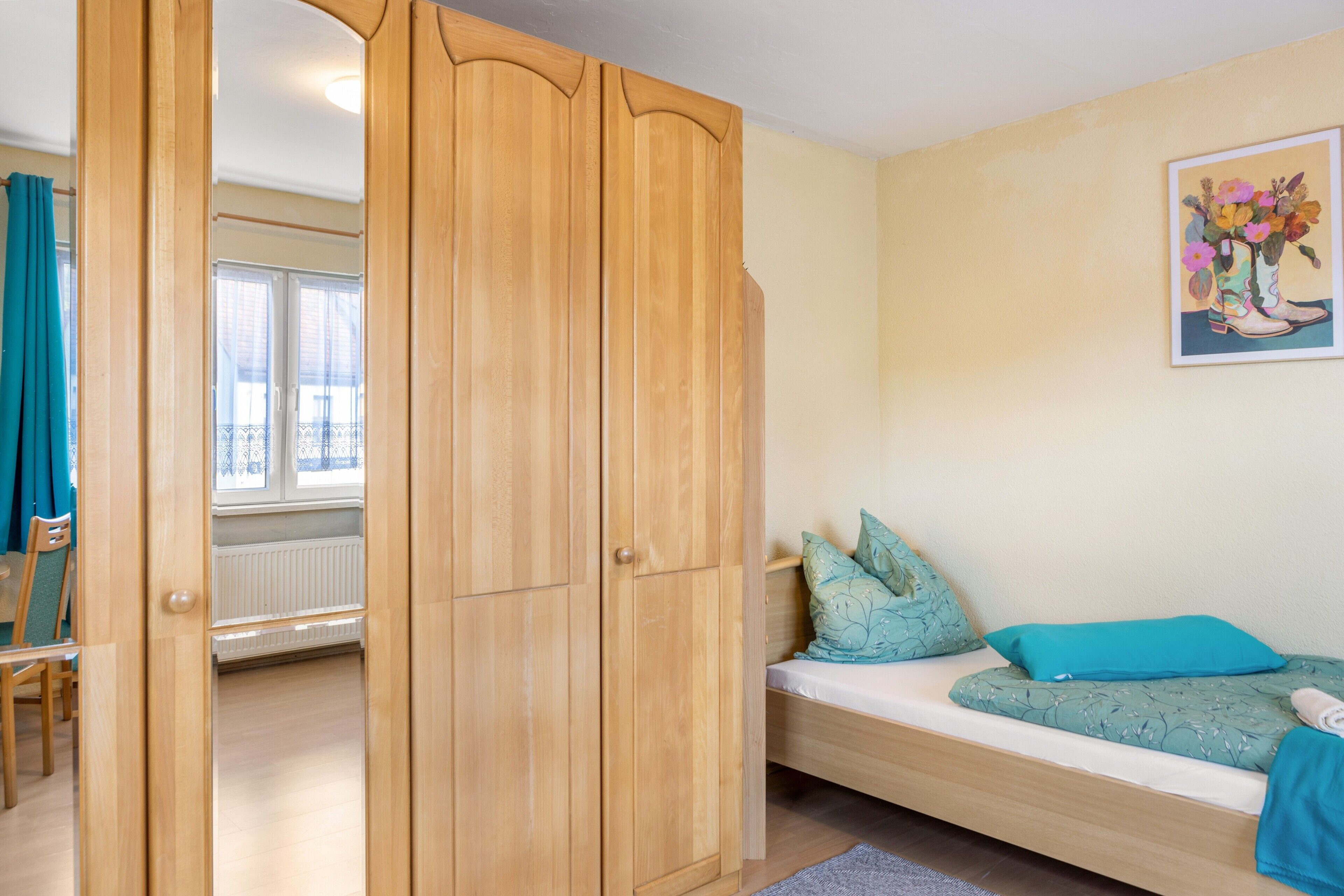 Une pièce avec une armoire en bois, un lit recouvert d’une couverture verte, une fenêtre et un radiateur.