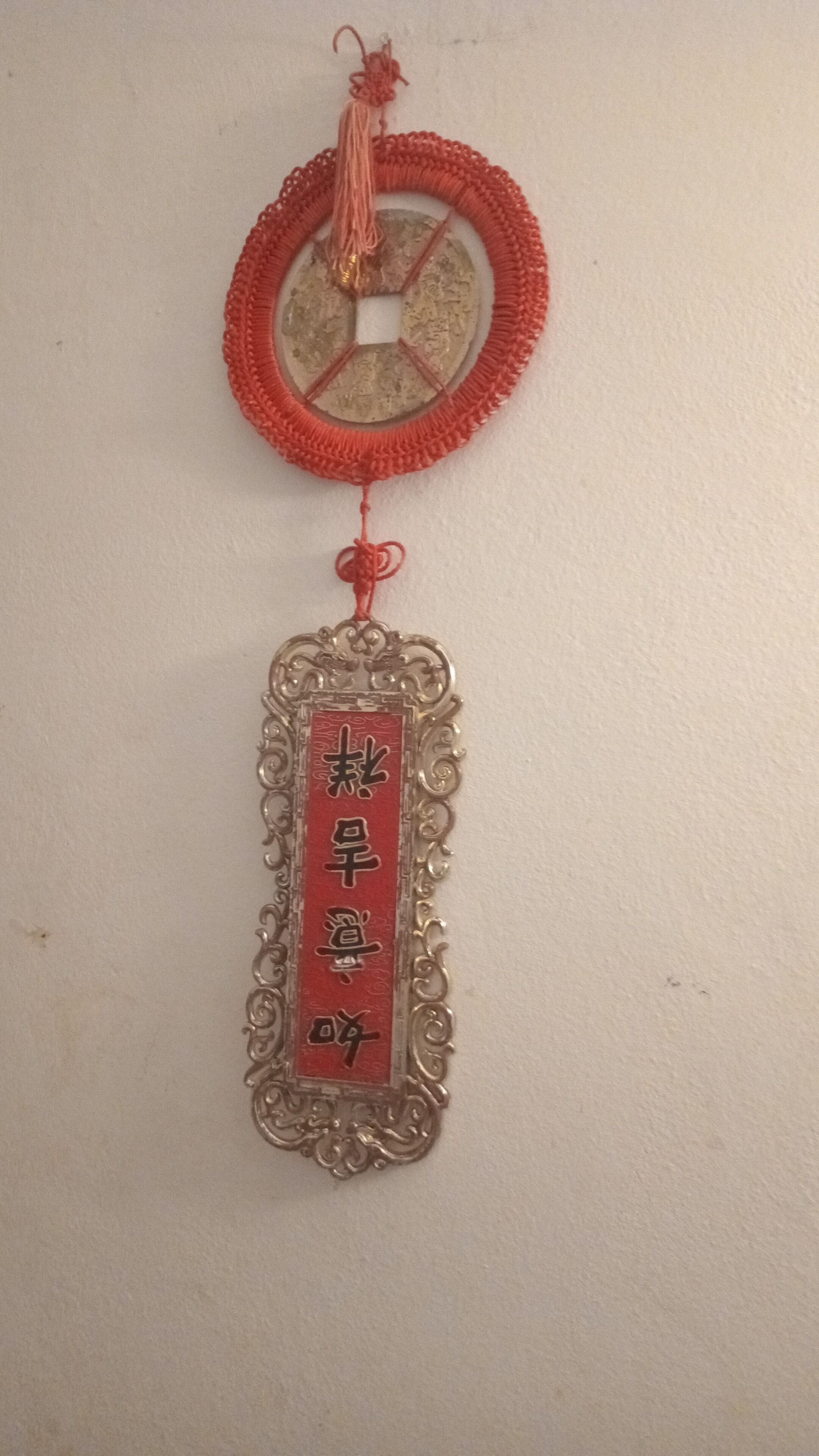 Een decoratief object aan de wand, met een rond bovenstuk en een rechthoekig onderstuk waarop Chinese karakters staan.