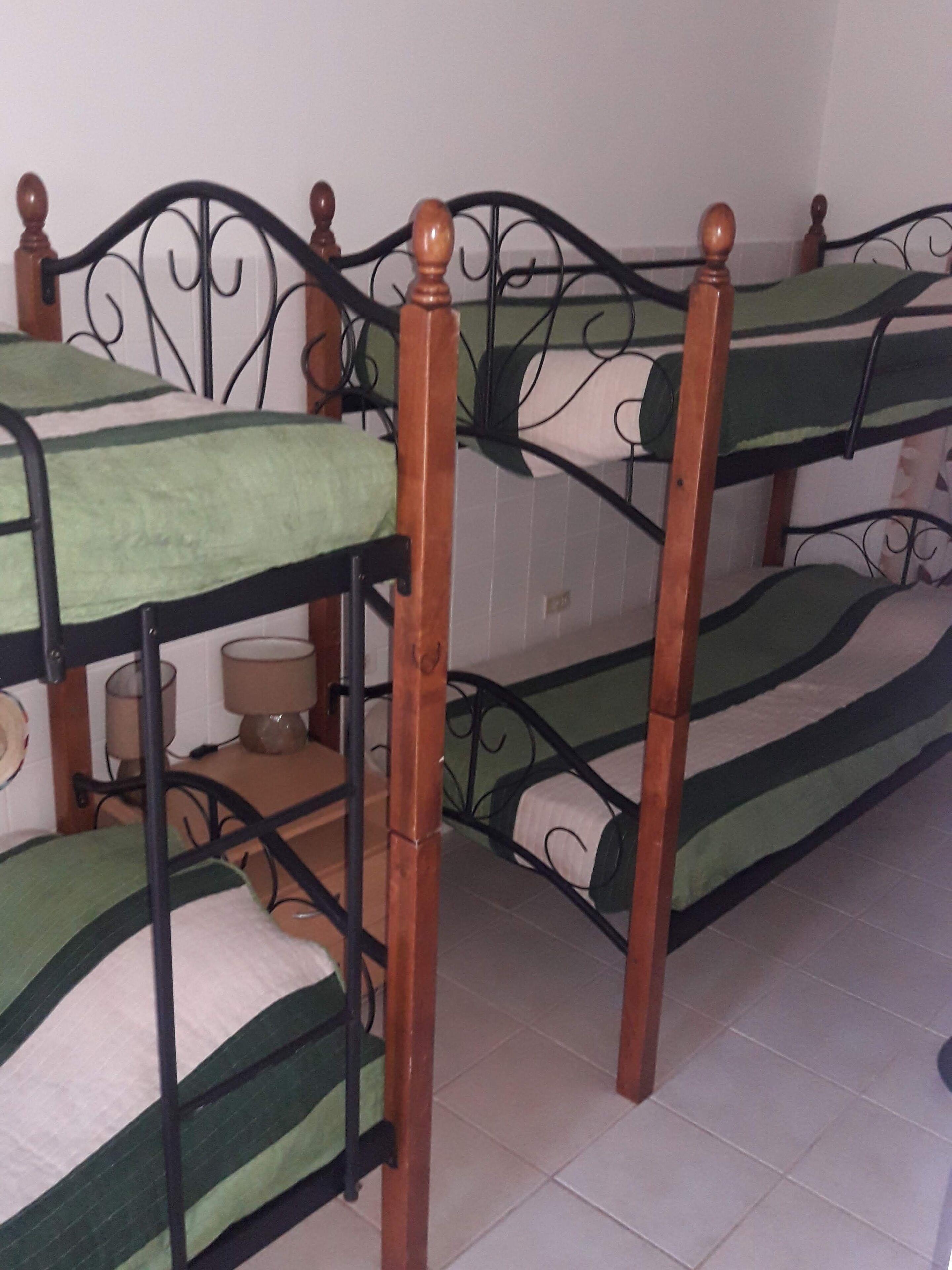 Una cama individual con dos literas, cabecera de madera, colcha verde y estructura metálica.