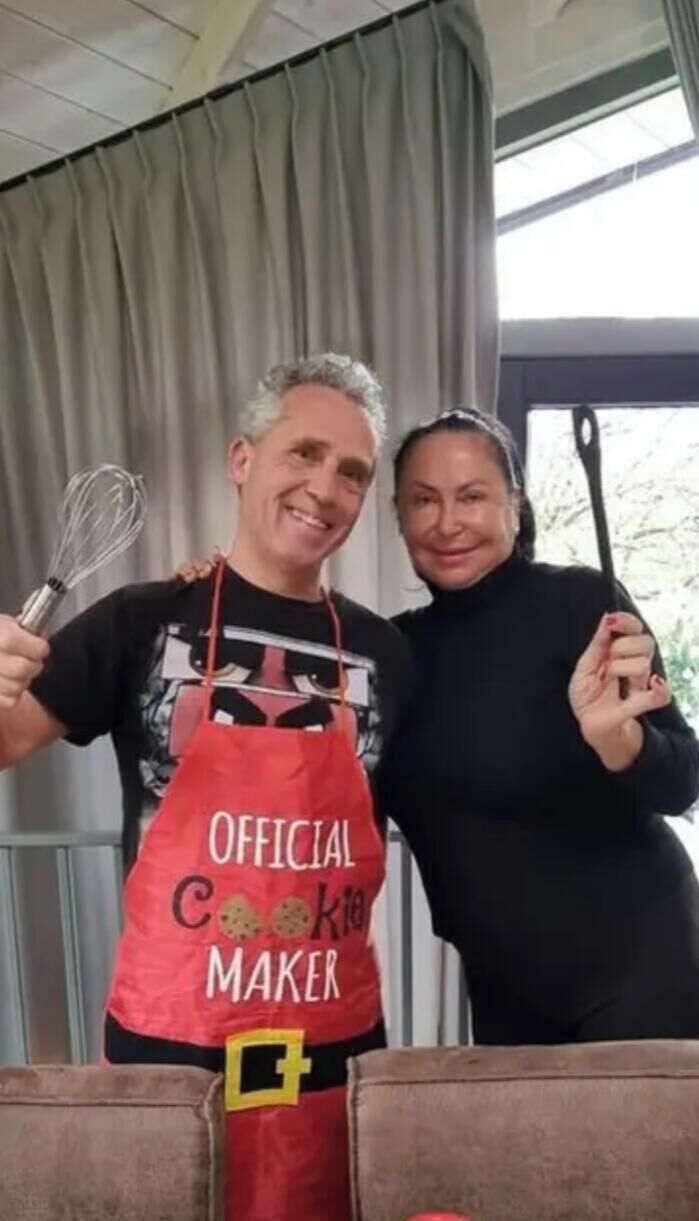 Eine Person hält einen Schneebesen und trägt eine rote Schürze mit dem Aufdruck 'OFFICIAL COOKIE MAKER'.