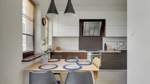 Une cuisine moderne avec un coin repas, comprenant une table en bois, des chaises grises et des luminaires suspendus.