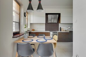 A modern kitchen with a dining area, featuring a wooden table, grey chairs, and pendant lights.