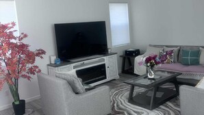 A modern living room with a flat-screen TV, grey sofas, a coffee table, and a potted plant. - Upscale Aurora Suite • Quiet, Private & Stylish (Aurora)