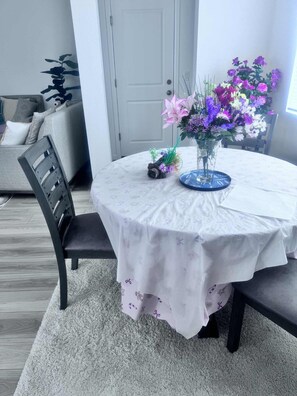Ein runder Esstisch mit weißer Tischdecke, eine Vase mit Blumen und ein Stuhl.