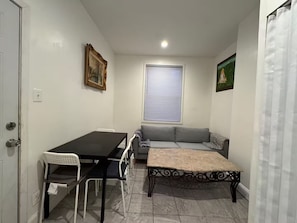 A small room with a dining table, chairs, a sofa, and a window with blinds.